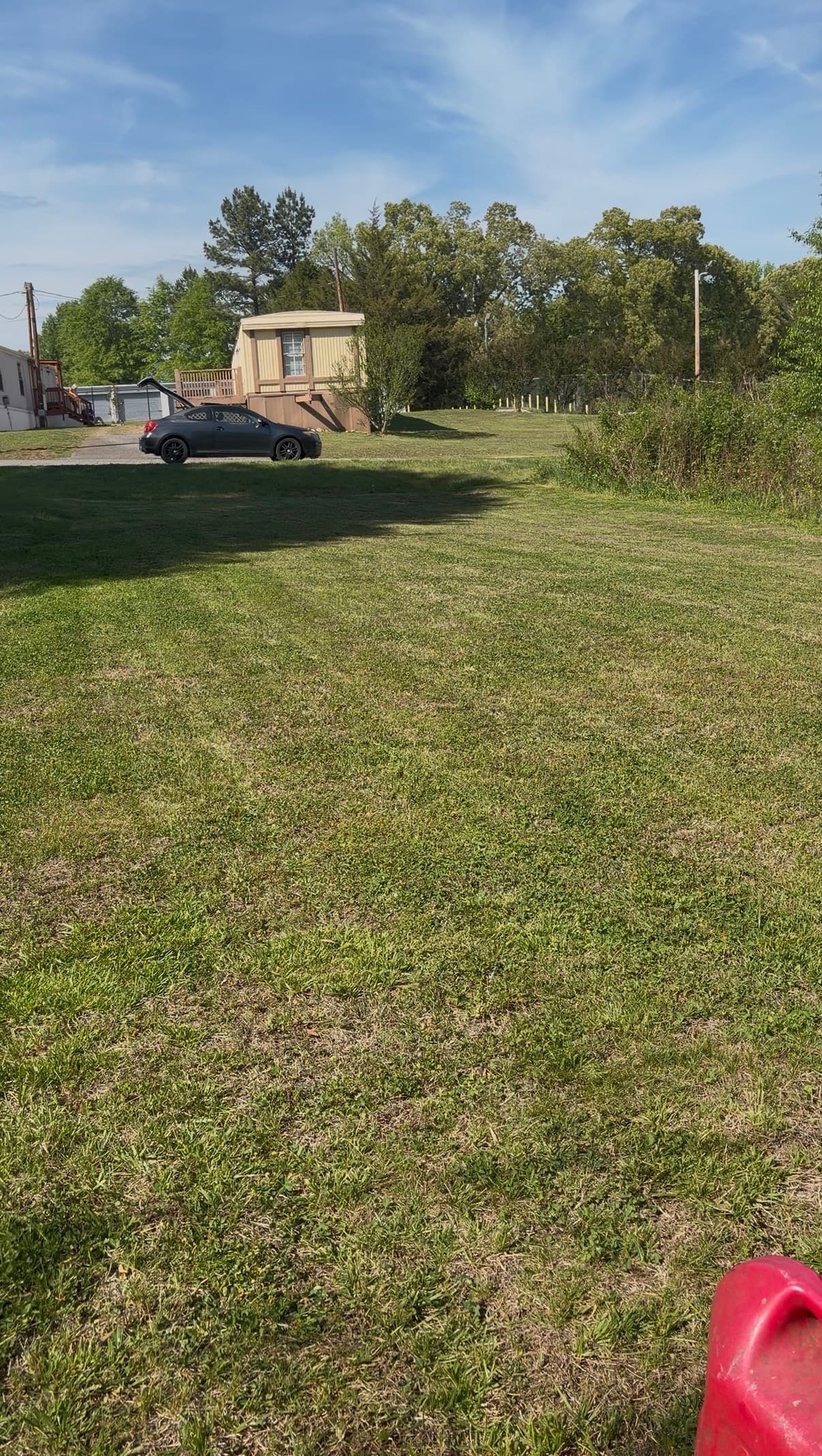 Dark grey car with open trunk parked near a mobile home on a large lawn.
