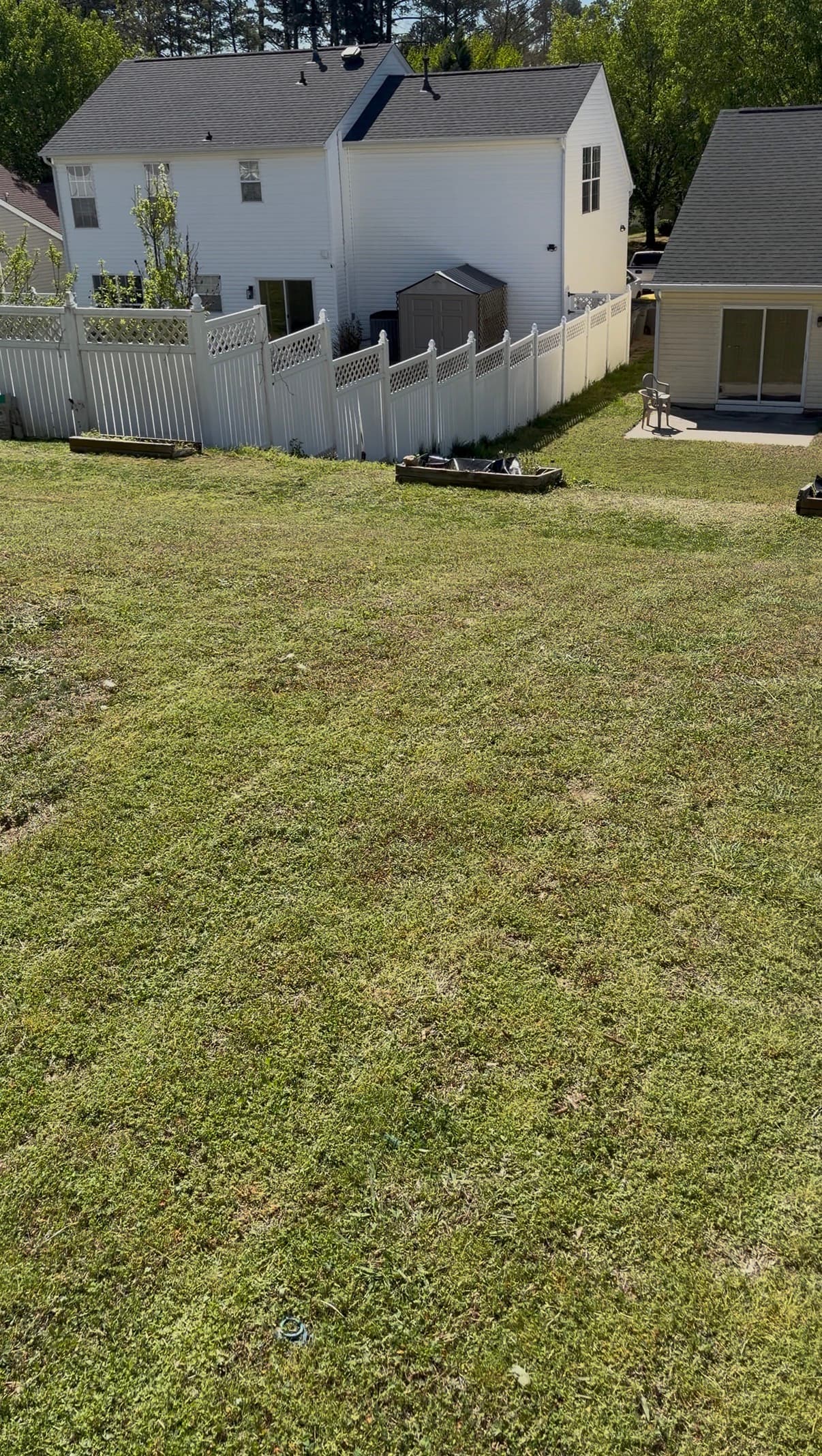 Sloping green lawn leading to a white vinyl fence and a two-story white suburban house.