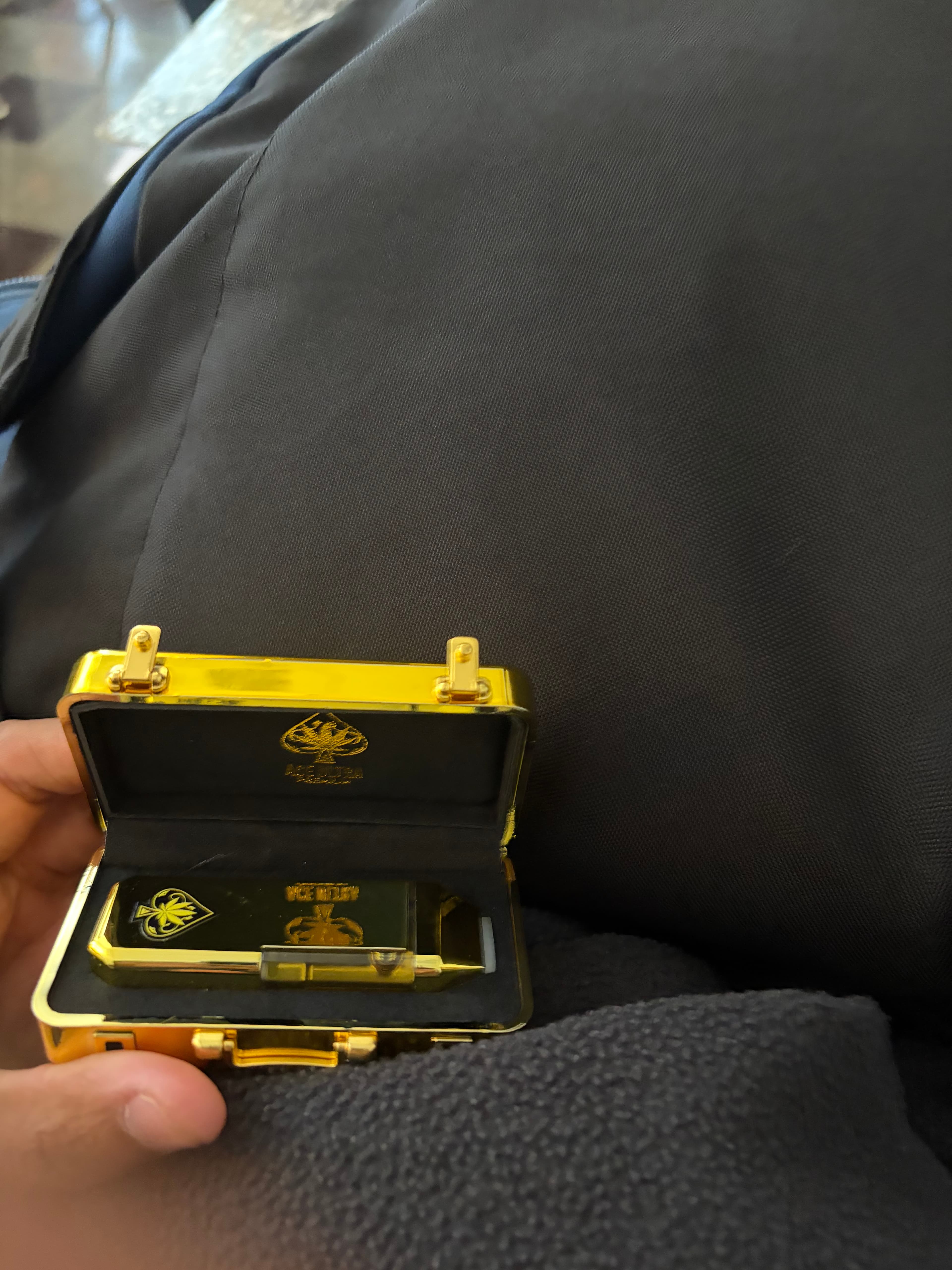 Open gold miniature briefcase containing a gold vape cartridge with spade logos, held by hand.