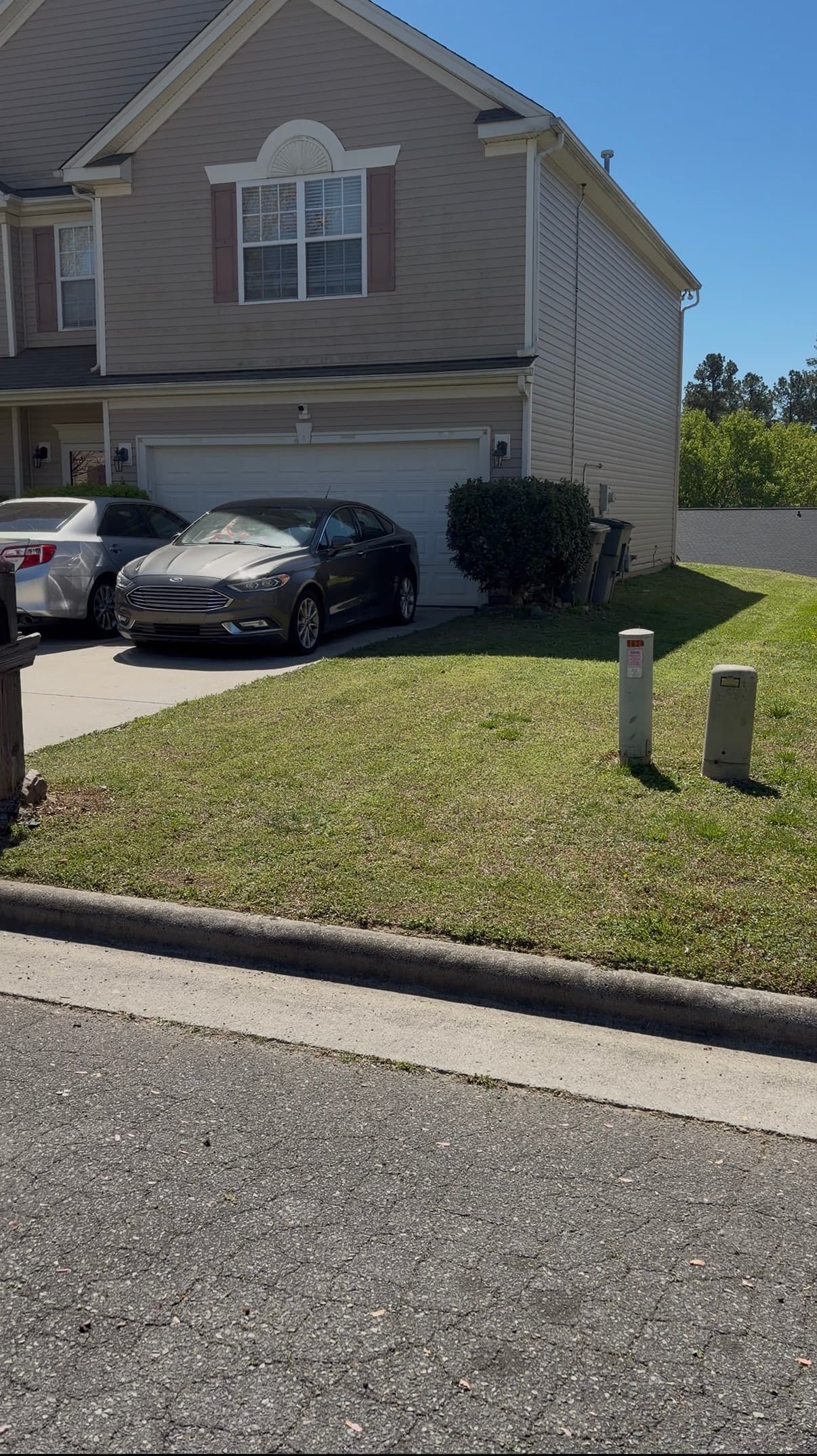 A gray sedan parked in the driveway of a suburban tan two-story home.